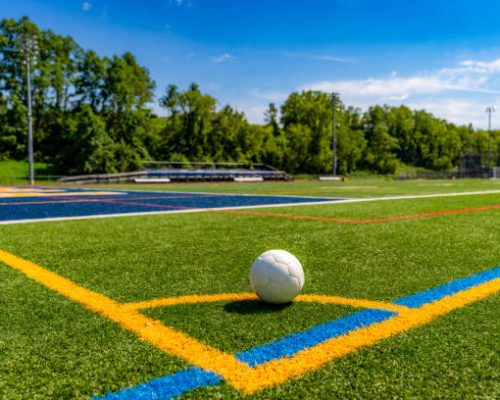 Afternoon photo of a white American soccer ball at the corner of a multi use synthetic turf field.